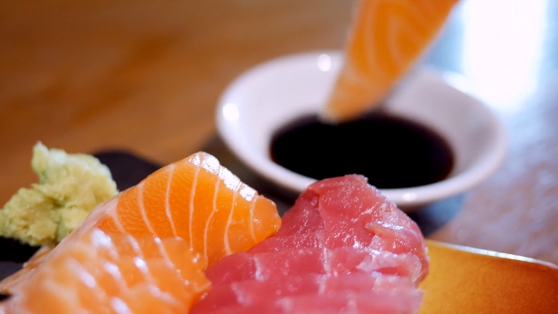 Close-up of salmon and tuna sashimi with one slice dipped in soy sauce