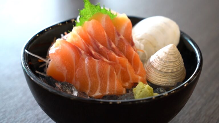 A black bowl filled with salmon sashimi slices on ice with wasabi and clams, illustrating is sashimi healthy in a fresh serving