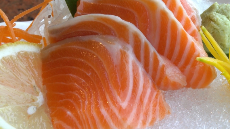 Close-up of salmon sashimi slices served on ice with lemon and wasabi