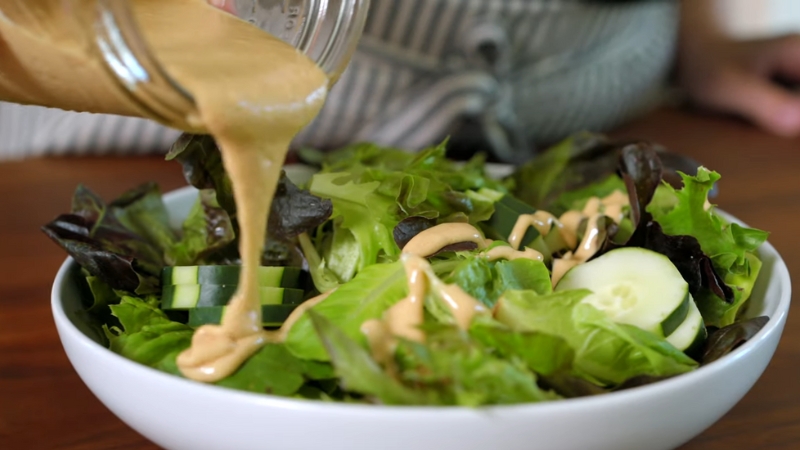 A Person Pouring Homemade Healthy Salad Dressing Over a Bowl of Fresh Greens and Vegetables